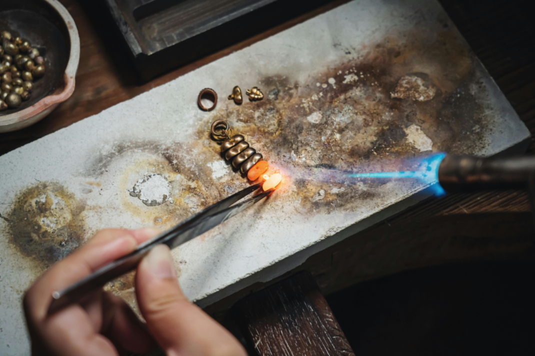 Artisan metalsmith working at a small jewelry bench in a Portland studio, carefully crafting a ring by hand, cover image for an Own Your Bloom story about makers scaling their craft without losing the handmade soul.
