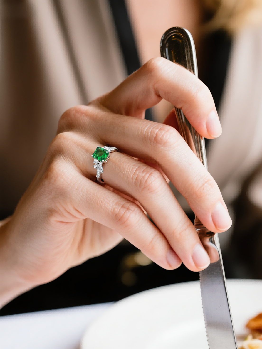 Customer wearing emerald cut green gemstone diamond ring while dining, luxury fine jewelry for women