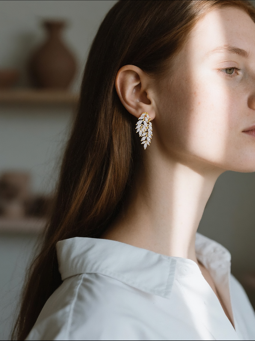 Customer wearing 14K gold leaf shaped diamond earrings, elegant indoor scene, women’s statement style