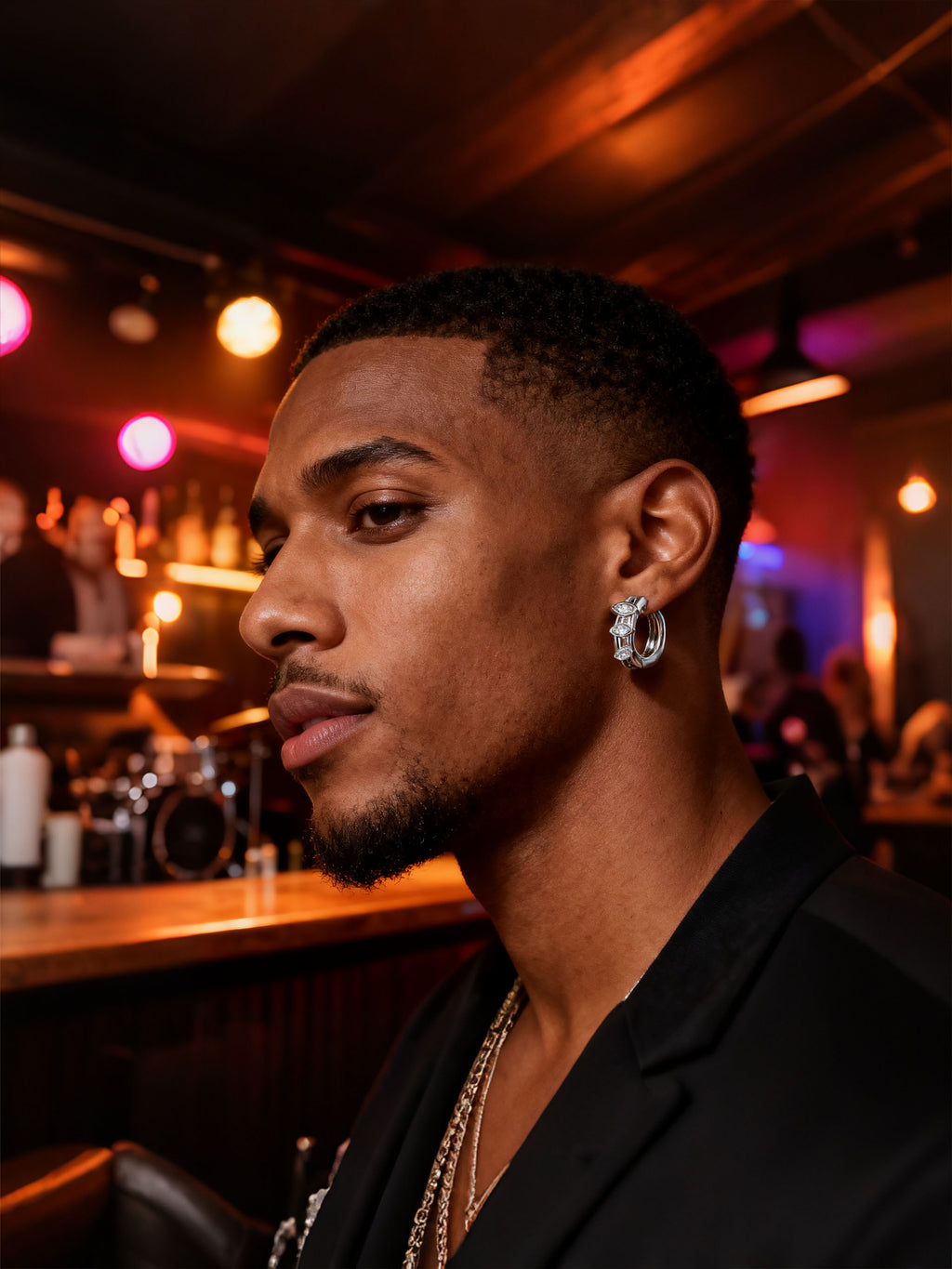 Man wearing Own Your Bloom 14K white gold marquise diamond hoop earrings, night bar portrait with warm lights, Houston.
