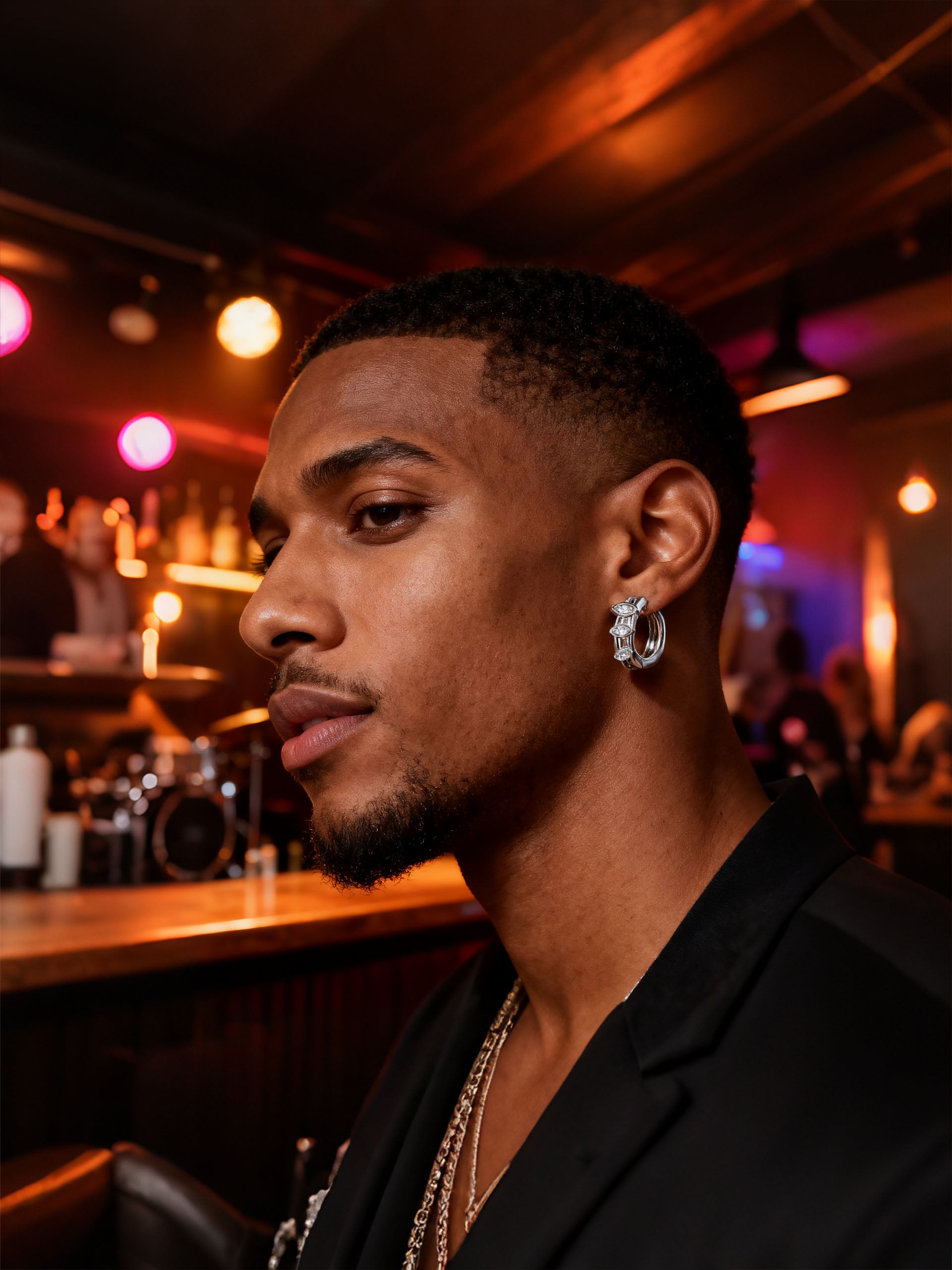 Man wearing Own Your Bloom 14K white gold marquise diamond hoop earrings, night bar portrait with warm lights, Houston.