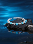 Own Your Bloom blue sapphire tennis bracelet displayed on black stone over water, luxury reflection and serene elegance, Miami.