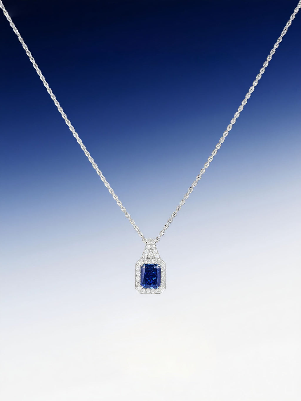 Own Your Bloom radiant blue sapphire halo pendant displayed against gradient blue background, symbolizing sophistication and luxury, Miami.