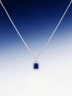Own Your Bloom radiant blue sapphire halo pendant displayed against gradient blue background, symbolizing sophistication and luxury, Miami.