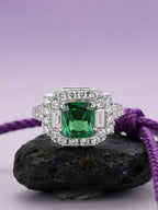 Own Your Bloom emerald halo baguette ring displayed on black stone with purple rope accent, elegant fine jewelry composition, Miami.