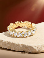 Own Your Bloom gold marquise and round moissanite eternity ring displayed on beige surface under warm light, luxury jewelry, Miami.