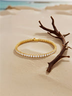 Own Your Bloom Radiant Rhythm Gold Tennis Bracelet resting on beach setting, symbolizing timeless sparkle and refinement, Boston.