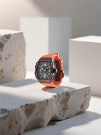 Own Your Bloom men’s skeleton automatic watch with orange strap displayed on stone pedestal, lifestyle studio scene, Los Angeles.