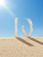 Own Your Bloom baguette moissanite hoop earrings showcased with blue sky and architectural background, chic minimalist style, Dallas.