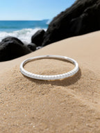 Own Your Bloom moissanite bangle tennis bracelet displayed on seaside rocks with ocean background, radiant fine jewelry, Miami.