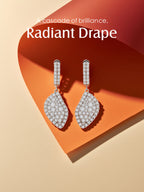 Own Your Bloom moissanite radiant drape drop earrings displayed on golden-orange background, luxurious fine jewelry radiating brilliance, Miami.