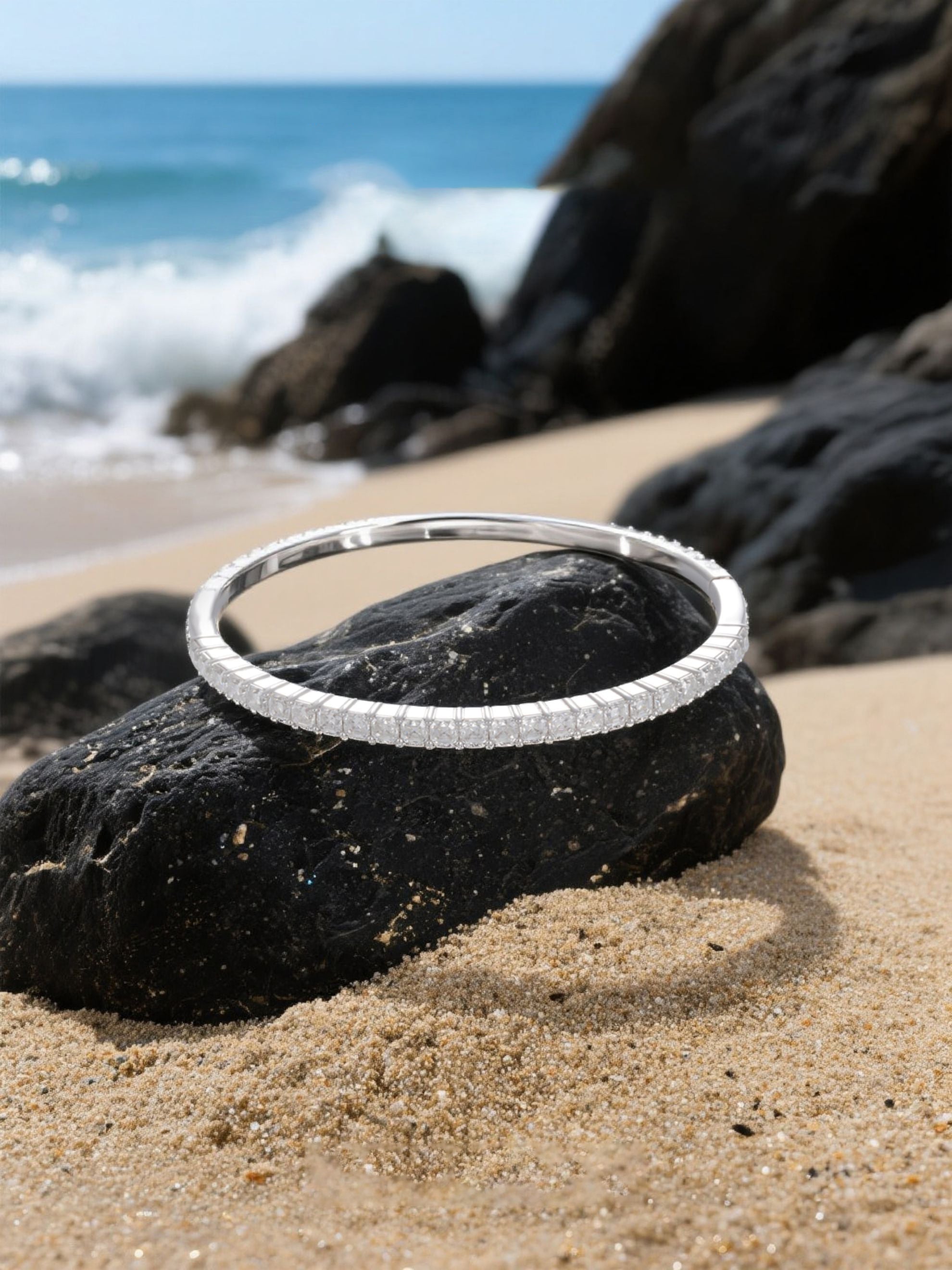 Own Your Bloom moissanite bangle bracelet placed on sand and rock with gentle sunlight reflections, elegant summer jewelry, Dallas.