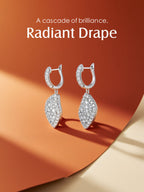 Own Your Bloom radiant drape moissanite earrings displayed on abstract orange backdrop with gentle shadow play, fine jewelry artistry, Boston.