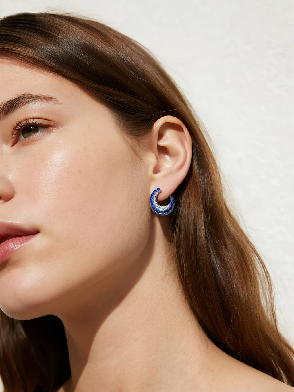 Own Your Bloom sapphire hoop earrings worn by woman outdoors, luminous gemstones sparkling under sunlight, Miami.
