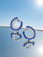 Own Your Bloom sapphire hoop earrings showcased under clear blue sky background emphasizing elegance and luxury, Dallas.