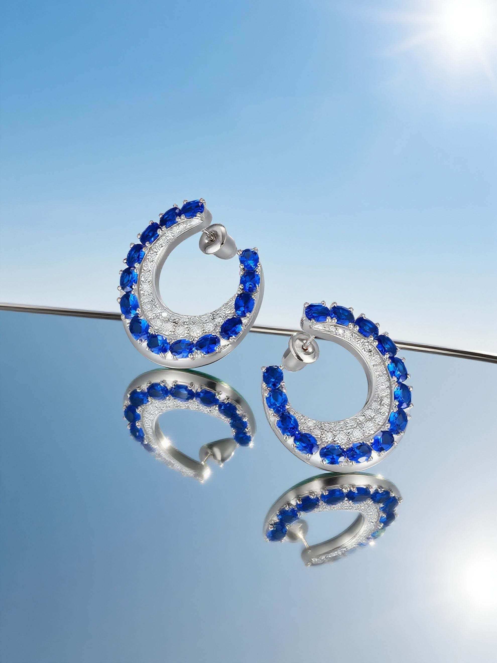 Own Your Bloom sapphire hoop earrings showcased under clear blue sky background emphasizing elegance and luxury, Dallas.