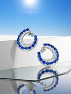 Own Your Bloom sapphire hoop earrings arranged on reflective surface with modern daylight aesthetic, Boston.