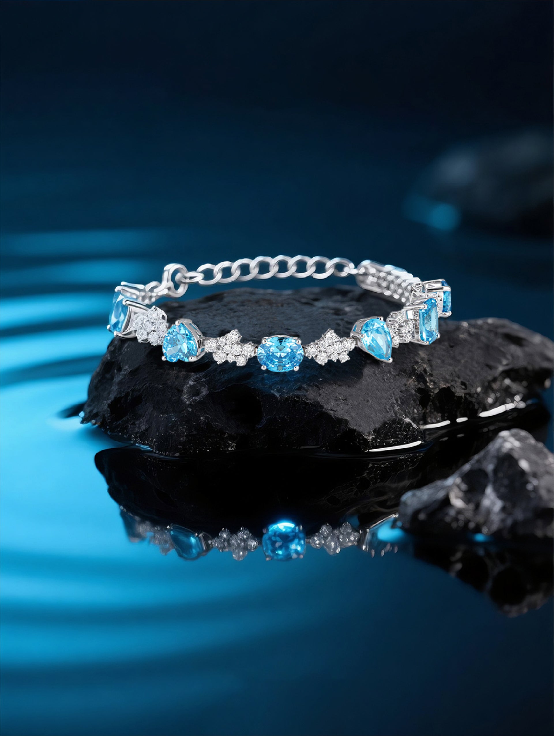 Own Your Bloom blue sapphire tennis bracelet resting on textured black rock with water reflection, modern elegance, Boston.